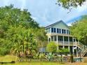 Inviting back exterior showcasing lush landscaping, marsh views, and a multi-story screened porch, ideal for outdoor living at 8869 Marsh Aire Ln, Edisto Island, SC 29438