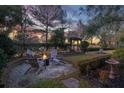 Cozy backyard fire pit area surrounded by mature trees, a garden, and well-manicured landscaping at 15 Watroo Pt, Daniel Island, SC 29492