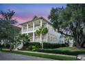 Charming two-story home featuring double porches, a landscaped yard with palm trees, and a classic coastal design at twilight at 164 River Green Pl, Charleston, SC 29492