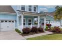 Home exterior featuring a covered front porch, an attached garage, flowering plants, and well-manicured landscaping at 149 Calm Water Way, Summerville, SC 29486