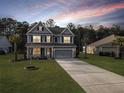 Beautiful two-story home with manicured lawn and palm trees, long driveway leading to garage at dusk at 502 Pontoon Rd, Huger, SC 29450