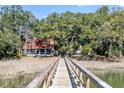 A wooden pier leads to a charming home with red roof and white siding surrounded by lush trees at 127 Oak St, McClellanville, SC 29458