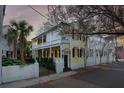 Charming two-story house with a yellow exterior, a white porch, and a wrought iron gate at 25 Logan St, Charleston, SC 29401