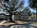 Two-story home with gray siding, white trim, and covered front porch beneath a mature shade tree at 343 Wappoo Rd, Charleston, SC 29407