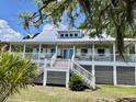 Charming elevated house featuring a spacious porch, white railings, and metal roof amidst lush greenery at 7753 Blue House Ln, Edisto Island, SC 29438