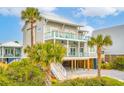 Lovely raised beach house exhibiting multiple balconies, a staircase to the ground level, and palm trees at 220 W Arctic Ave, Folly Beach, SC 29439