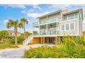 Gorgeous raised beach house showcasing a spacious outdoor entertaining area and vibrant tropical landscaping at 220 W Arctic Ave, Folly Beach, SC 29439