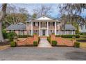 Beautiful two-story brick house boasts columns, lush landscaping, and a charming walkway leading to the front door at 12 Broughton Rd, Charleston, SC 29407