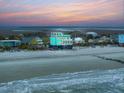 Expansive coastal view showcasing a turquoise beach house elevated on stilts, surrounded by sandy shores and neighboring homes at 1699 E Ashley Ave # B, Folly Beach, SC 29439