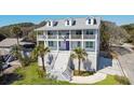 Stunning three-story coastal home featuring a white exterior, double balconies, and landscaped front yard at 502 W Ashley Ave, Folly Beach, SC 29439