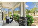 Cozy front porch featuring stone column bases, white columns, lush greenery, and a comfortable outdoor chair at 3000 Flat Rock Ln, Ridgeville, SC 29472