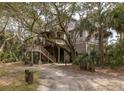 Exterior shot of a charming home with wooden siding, lush greenery, and a rustic staircase at 263 Pelican Flight Dr, 15.4% Share, Dewees Island, SC 29451