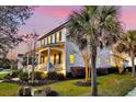 A side view of a two-story home, highlighting its well-lit windows, green lawn, and surrounding palm trees against a pink sky at 1525 Harriman St, Mount Pleasant, SC 29466