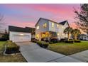 View of the home's back exterior, featuring a detached garage, a paved driveway, and a well-kept lawn at dusk at 1525 Harriman St, Mount Pleasant, SC 29466