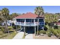 Charming raised beach house with a red roof, blue siding, and beautiful tropical landscaping at 716 E Arctic Ave, Folly Beach, SC 29439