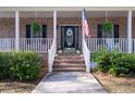 Close-up of a brick porch with a white railing, stairs leading to an arched front door with an American flag at 5367 Boone Run, Hollywood, SC 29449