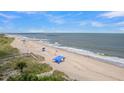 Beach view with dunes, wooden walkways, and scattered umbrellas in the sand, showing the proximity to the ocean at 1702 Palmetto Blvd, Edisto Island, SC 29438