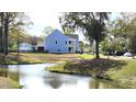 A charming blue home sits alongside a pond, featuring a quaint balcony, a well-kept lawn and attached garage at 1984 Shadetree Blvd, Johns Island, SC 29455