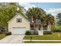 Inviting yellow home with a white garage door and a cozy front porch with palm trees at 225 Hanahan Plantation Cir, Hanahan, SC 29410