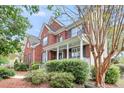 Side view of a red brick house featuring a covered front porch, mature trees, and lush landscaping at 1185 Out Of Bounds Dr, Summerville, SC 29485