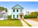 Charming two-story home with light blue siding, red door, landscaped yard and a concrete driveway at 1130 5Th Ave, Charleston, SC 29407