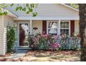 Close-up of the front door area with storm door, sidelight, shutters, and lush, pink flower bushes at 1411 River Front Dr, Charleston, SC 29407