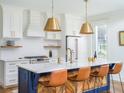 Stylish kitchen with white cabinets, a blue island with leather chairs, and brass pendant lighting at 2 Live Oak Ave, Charleston, SC 29407