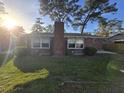 Exterior of a brick home showcasing a chimney, sunny backyard, and mature trees at 5937 Willard Dr, Hanahan, SC 29410