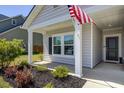 View of a cozy front porch with an American flag, lush landscaping, and a black front door at 117 Camellia Bloom Dr, Moncks Corner, SC 29461