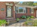 Inviting front porch area showcasing a decorated glass door, brick accents, and vibrant landscaping for added charm at 1421 Fairfield Ave, Charleston, SC 29407