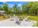 Stone backyard patio with a fire pit and four white adirondack chairs, surrounded by a lawn and mature trees at 481 Woodland Shores Rd, Charleston, SC 29412