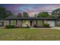 Inviting single-story brick home with a manicured lawn, updated paint, shutters, and attached garage at twilight at 7655 Ovaldale Dr, North Charleston, SC 29418