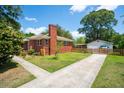 Rear view showing the brick home's chimney, driveway leading to detached garage, and fenced yard at 1915 Aichele Dr, North Charleston, SC 29406