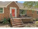 Close-up of the house entrance featuring a red door, brick steps and a small seating area at 13 Charlestowne Rd Rd, Charleston, SC 29407