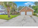 Brick home featuring a two-car garage and a long cracked driveway, surrounded by green grass and trees at 2120 Fife Ln, Charleston, SC 29414