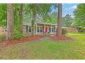 All brick home with red door and black shutters nestled among the trees in the front yard at 206 Jimbo Rd, Summerville, SC 29485