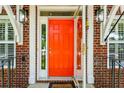 Close-up of the vibrant orange front door framed by stylish exterior sconces and brick detailing at 174 Revetment Ln, Mount Pleasant, SC 29464