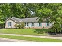 Inviting single-story brick home displaying light blue shutters, surrounded by lush, mature trees and manicured front lawn at 1673 Sulgrave Rd, Charleston, SC 29414