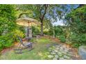 Tranquil backyard patio with a table, chairs, umbrella, and stone pathway amidst green foliage at 318 N Magnolia St, Summerville, SC 29483