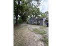 View of backyard with trees and gravel, showing the exterior of the gray, single-story home at 715 Yew St, Charleston, SC 29407