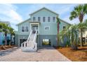 Inviting two-story beach home featuring a brick driveway, lush palm trees, and an appealing coastal color palette at 313 E Arctic Ave, Folly Beach, SC 29439
