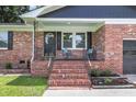 Inviting brick porch with decorative chairs, black shutters, and white trim, a lovely entrance at 6305 Lucille Dr, North Charleston, SC 29406