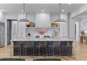 Bright, open kitchen with a large marble island, modern pendant lighting, and white cabinetry provides a sleek and stylish aesthetic at 27 Watroo Pt, Daniel Island, SC 29492