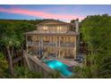 Elegant three-story home with a private pool and deck, illuminated at dusk, showcasing outdoor living spaces at 43 Surfsong Rd, Kiawah Island, SC 29455