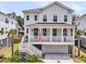 A charming two-story white home with a welcoming porch adorned with flags and palm trees in the yard at 1494 N Lakeshore Dr, Mount Pleasant, SC 29466