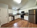Modern kitchen boasts stainless steel appliances, white cabinetry, laminate countertops, and wood flooring at 1705 Falcon Cove Ln, Hanahan, SC 29410