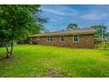 Backyard view of this single-story home with a large grass area, brick exterior, and fenced perimeter at 2003 Savage Rd, Charleston, SC 29407