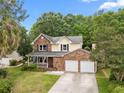 Charming brick home with two-car garage, covered porch, and mature trees on a sunny day at 5488 Altamaha Dr, North Charleston, SC 29420
