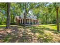 A sprawling brick home is surrounded by mature trees with a covered porch, offering a blend of comfort and style at 6385 Shilelagh Oaks Pkwy, Ravenel, SC 29470