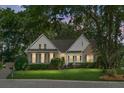 Evening view of charming brick home featuring a well-manicured lawn, and mature trees, creating an inviting curb appeal at 652 Spinner Cir, Mount Pleasant, SC 29464
